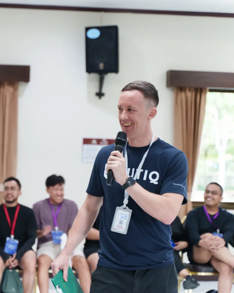 Phill Savage, Event Director for the Offsite Thailand program, smiling and holding a microphone while facilitating an in-person team workshop as participants laugh behind him